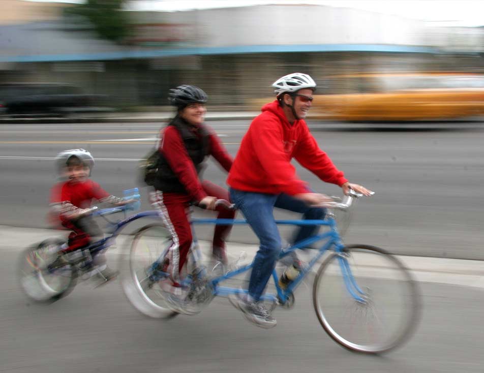 A family riding a tandem bike with a tag along